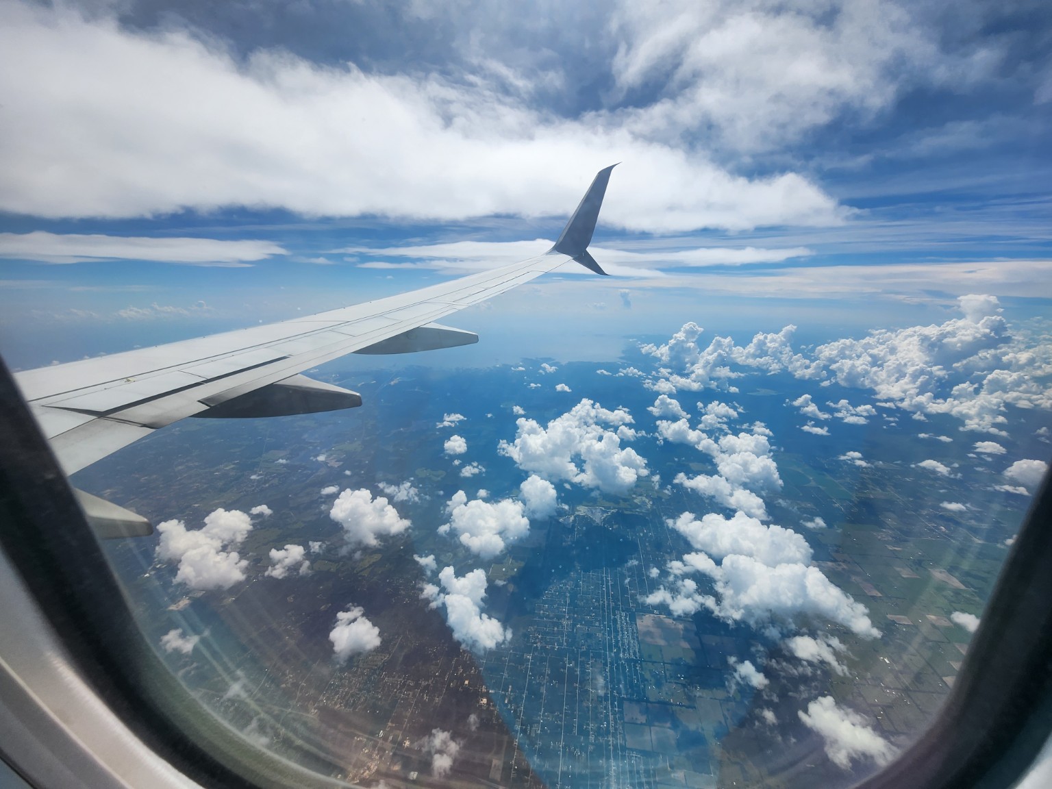 Airplane wing above clouds and a patchwork landscape.